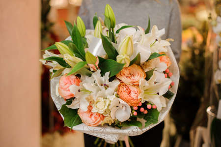 woman in gray sweater holds a bouquet white lilies, white orchids, beige pion-shaped roses in wrapping paperの写真素材