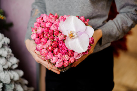 elegant woman in gray sweater holds a bouquet with many small pink roses and one big white orchidの写真素材