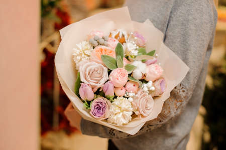 woman in gray sweater holds a big bouquet with pink and purple roses, apricot pion-shaped roses and eucalyptus in pink wrapping paperの写真素材