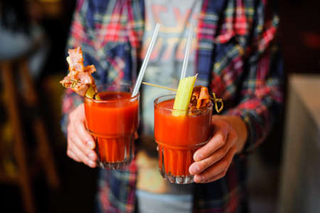 guy in the plaid shirt is holding two glasses of alcoholic cocktail Bloody Mary indoorsの写真素材