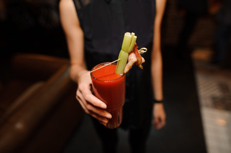thin female in the black shirt holding a glass of alcoholic cocktail Bloody Mary indoors