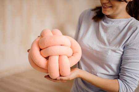 Woman in a grey shirt holding a cute peach colored knot pillow on the indoors background