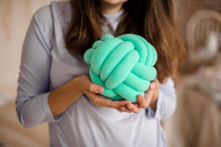 Woman in a grey shirt holding a cute turquoise knot cushion on the indoors background