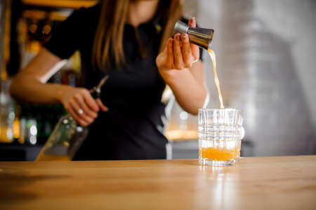 barista prepares a cocktail and pours orange juice with a thin trickle into a crystal glassの写真素材
