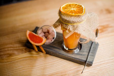 cocktail decorated with a slice of dried orange on a special wooden stand with a spoon, a grapefruit slice, cinnamon and candiesの写真素材
