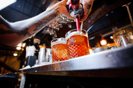 barman with tattoos on his arms pours fresh beer from a barrel into glasses behind the bar counterのeditorial素材