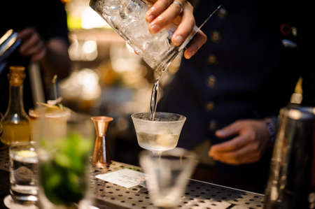 Barman pouring fresh and cold alcoholic drink into the cocktail glass on the bar counterの写真素材