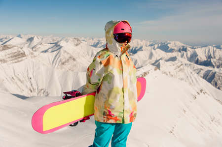 Portrait of female snowboarder in sportswear standing on the mountain peak against the scenic backgroundの写真素材