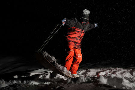 Snowboarder dressed in the orange sportswear balancing on the board at the dark snowy nightの写真素材