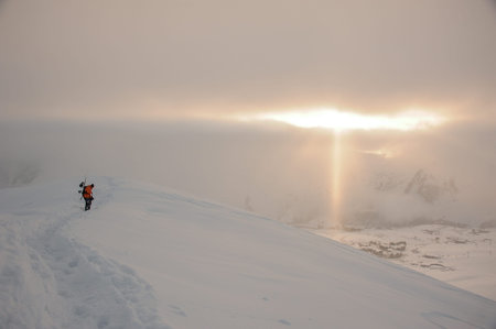 Snowboarder walking on the high mountain peak covered with snow under the golden sun raysの写真素材