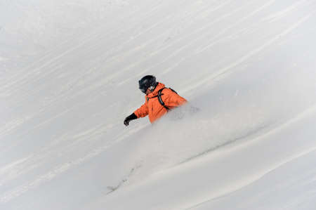 Male snowboarder dressed in sportswear riding down the snow slope on the bright sunny dayの写真素材