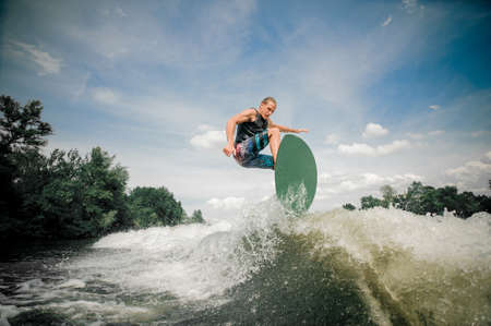Sporting wake boarder rides up the wake and the energy of the wake launches him airborneの写真素材