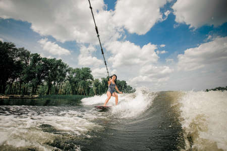 Young slim brunette athletic wet woman wake boarding down the river enjoying her excitement summer vacationの写真素材