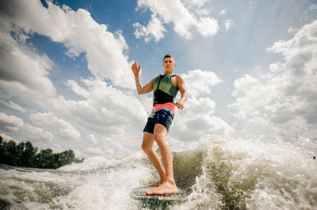 Athletic healthy man rides the waves in a summer river,having fun on the background of the beautiful cloudsの写真素材