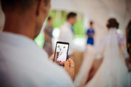 Back view of man recording a video of dancing bridegroom and bride on the wedding party using a smartphoneの写真素材