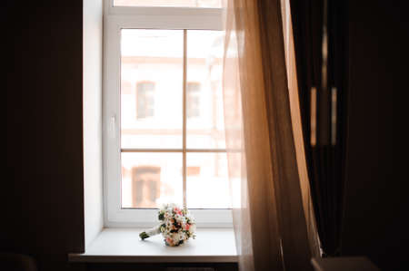 Beautiful and pretty wedding bouquet of flowers on the white window sill in the dark roomの写真素材