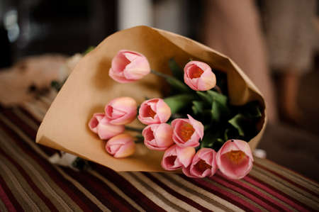 Beautiful bouquet of pretty and tender pink tulips in a kraft paper on the bedの写真素材