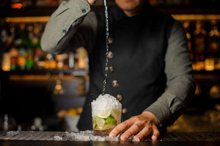 Barman pouring cachaca into the cocktail glass making a fresh Caipirinha cocktail on the bar counterの写真素材