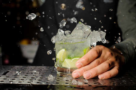 Bartender hand holding a glass filled with fresh and cool Caipirinha cocktail on the bar counterの写真素材