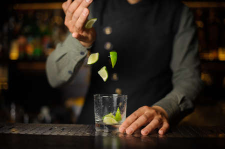 Bartender adding pieces of lime into the cocktail glass making a fresh Caipirinha cocktail on the bar counterの写真素材