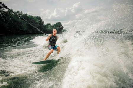 Young and athletic man wakesurfing on the board against the skyの写真素材