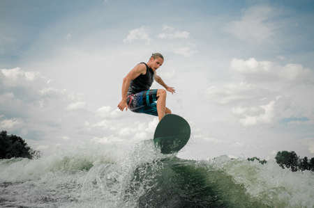 Young and athletic guy wakesurfing on the board down the river against the skyの写真素材