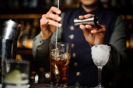 Bartender making a cocktail stirring it in a glass with ice cubes on the bar counterの写真素材