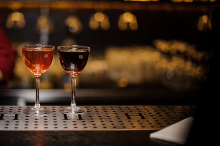 Two elegant cocktail glasses filled with the alcoholic drinks arranged on the bar counter against blurred backgroundの写真素材
