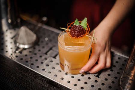 Woman hand holding a glass filled with a fresh orange decorated with a candy alcoholic cocktailの写真素材
