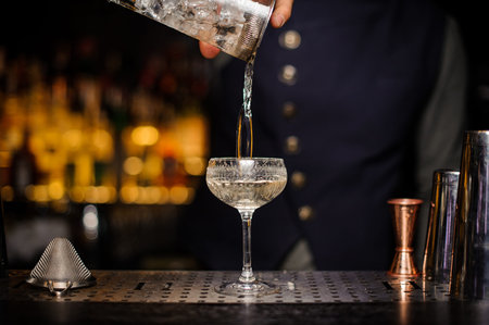 Bartender pouring a ready alcoholic drink with ice cubes into the cocktail glass on the bar counterの写真素材