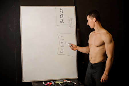 Sexy muscular personal trainer practicing crossfit stands and writes of the board using a markerの写真素材