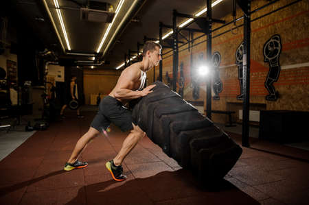Sexy and muscular young man practicing crossfit flipping a large tire at the sports hallの写真素材
