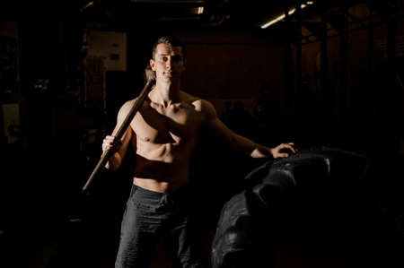 Sexy and muscular young man holding a heavy hammer near the large tire at the gymの写真素材