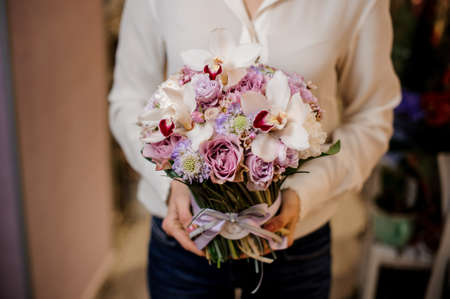 Woman dressed in a white blouse holding a beautiful bouquet of tender and colorful flowers tied with a pretty ribbonの写真素材