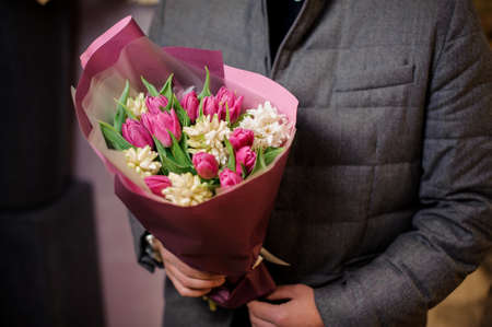 Man dressed in a grey jacket holding a beautiful pink bouquet of flowers consisting of tender tulipsの写真素材