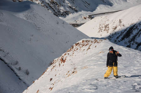 Freeride male snowboarder standing on the mountain peak covered with snow on the sunny dayの写真素材