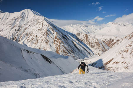 Freeride male snowboarder walking on the mountain slope covered with snow on the sunny dayの写真素材