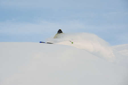 Professional male snowboarder in sportswear sliding down on the powder snow covering mountain slope on the bright dayの写真素材
