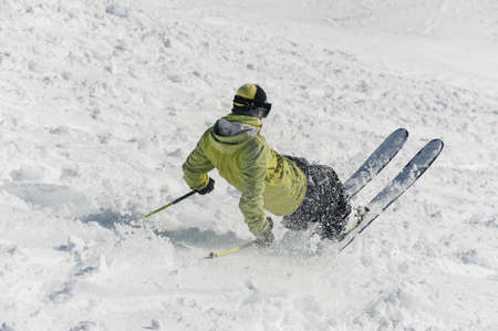 Back view of male freeride skier dressed in green sportswear sliding down the snowy hillの写真素材