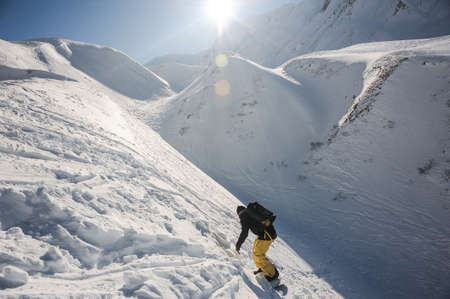 Freeride snowboarder sliding on the snowy mountain slope under the brightly shining sun in the blue skyの写真素材