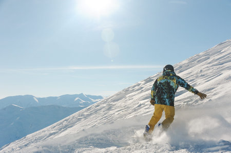 Back view of male freeride skier dressed in sportswear sliding down the snowy hill against the blue skyの写真素材