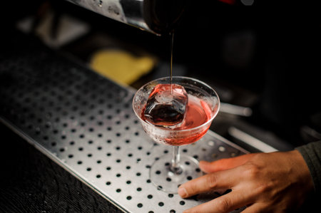 Bartender serving an adorable fresh alcoholic red cocktail with an ice on the steel gray bar counter