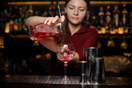 Professional bartender girl pouring an adorable red cocktail into the glass at the steel bar counterの写真素材