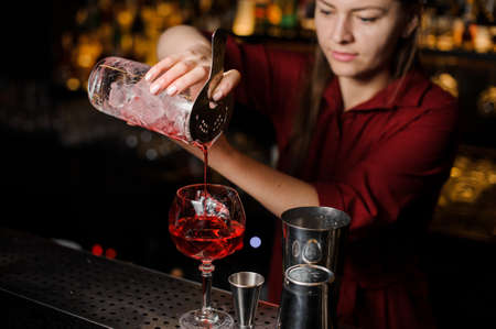 Professional bartender girl pouring a light red cocktail into the glass at the steel bar counterの写真素材