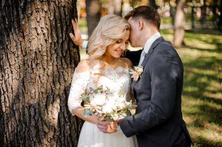 Portrait of a young bridegroom kissing a lovely blonde bride holding a beautiful bouquet of flowersの写真素材