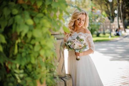 Beautiful blonde bride dressed in a lovely wedding dress holding a tender bouquet of flowersの写真素材