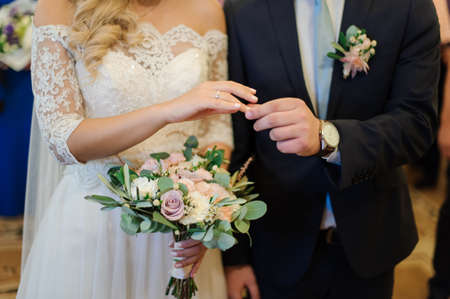 Bridegroom putting a wedding ring on the blonde bride finger standing in the wedding palaceの写真素材