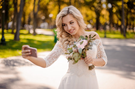 Lovely blonde bride dressed in a beautiful wedding dress holding a tender bouquet of flowers and...