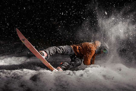 Man dressed in orange and black sportswear shockingly snowboarding in the dark under the snowの写真素材