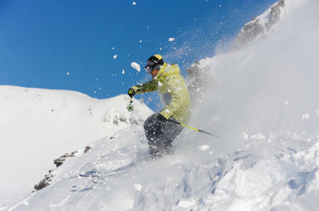 Skier dressed in yellow and grey sportswear running down the slope on the background of Gudauri, Georgiaの写真素材